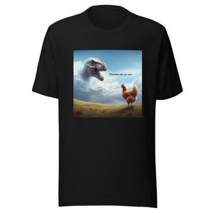 May include: Black t-shirt featuring a graphic of a dinosaur and a chicken. The dinosaur is in the background and the chicken is in the foreground. The text "Remember who you are!" is printed on the t-shirt.