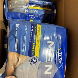 以下が含まれることがあります： 段ボール箱に入ったTENA男性用保護下着の2つのパッケージ。パッケージは青とグレーで、「MEN」の文字が大きく表示されています。パッケージにはXL TGと記載されており、ウエストサイズは114〜147cmです。