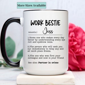 May include: White ceramic mug with a black handle. The mug has a black rim and the text "WORK BESTIE Jess noun(n.) 1.)Some one who makes every day better by understanding every eye roll and eyebrow raise. 2.)The person who will seek you out immediately to relay any and all work place drama. 3.)The one who was first your colleague and now is your friend See also: Partner in crime" printed on it.