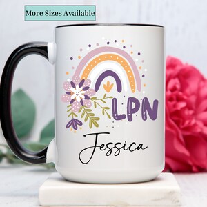 May include: White ceramic mug with a black handle. The mug features a rainbow with purple, orange, and pink colors, a floral design, and the text "LPN Jessica".