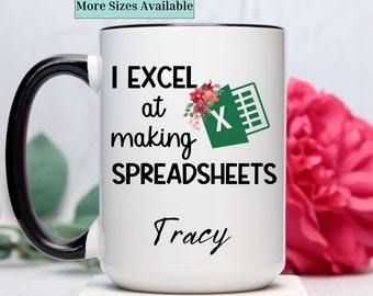 May include: White coffee mug with a black handle. The mug has a green and white Excel logo with flowers and the text "I EXCEL at making SPREADSHEETS Tracy".
