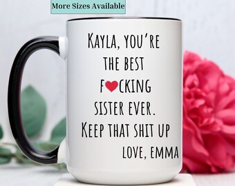 May include: White ceramic coffee mug with a black handle. The mug has black text that reads "KAYLA, YOU'RE THE BEST FOCKING SISTER EVER. KEEP THAT SHIT UP LOVE, EMMA". A red heart is in the word "FOOKING".