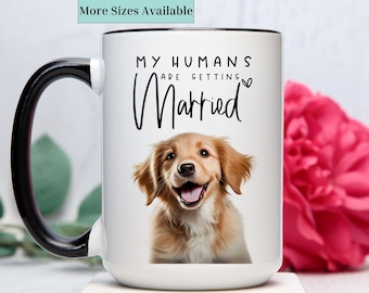 May include: White ceramic coffee mug with a black handle. The mug has a picture of a golden retriever puppy with the text "My humans are getting married" printed on it.