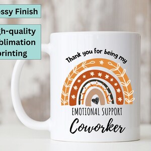 May include: White ceramic mug with a rainbow design and the text "Thank you for being my Emotional Support Coworker".