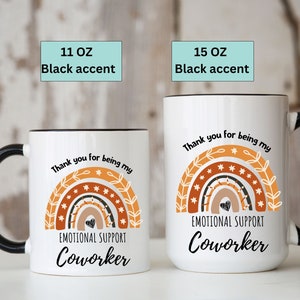May include: White ceramic mug with a black rim and handle. The mug features a rainbow design with stars and the text "Thank you for being my Emotional Support Coworker". The mug is available in 11 oz and 15 oz sizes.