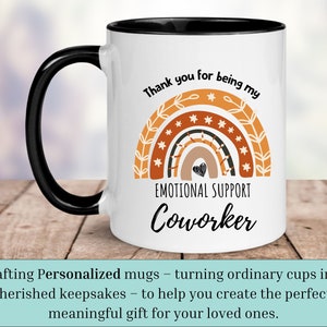 May include: White ceramic coffee mug with a black handle and black rim. The mug features a rainbow design with stars and the text "Thank you for being my Emotional Support Coworker".