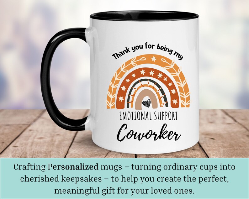 May include: White ceramic coffee mug with a black handle and black rim. The mug features a rainbow design with stars and the text "Thank you for being my Emotional Support Coworker".