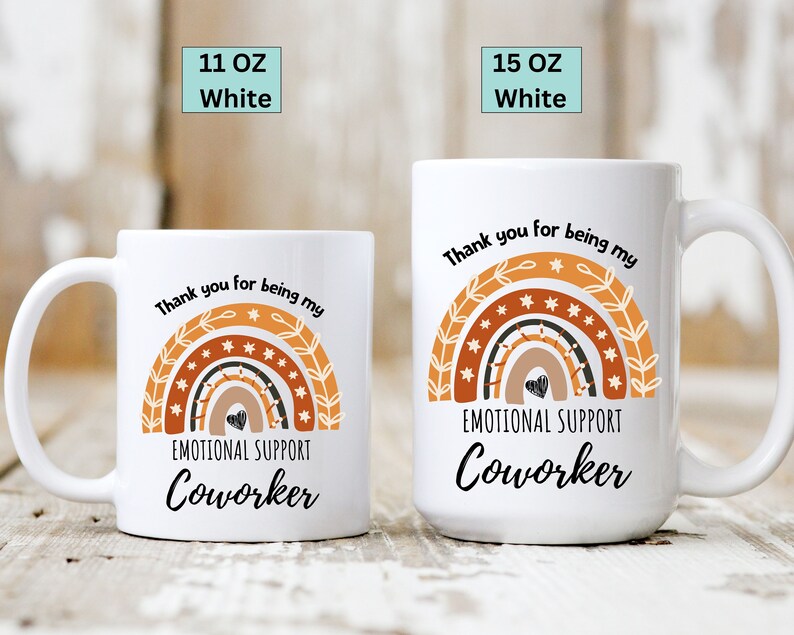 May include: White ceramic coffee mug with a rainbow design and the text "Thank you for being my Emotional Support Coworker".