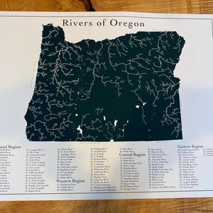 Peut inclure: Une impression cartographique intitulée "Rivers of Oregon" présente une silhouette vert foncé de l'État avec des lignes blanches représentant les rivières. L'impression comprend des listes de rivières classées par région.