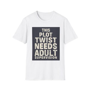 May include: A white short-sleeved t-shirt featuring a centered dark gray rectangular graphic. The graphic contains the distressed white text: THIS PLOT TWIST NEEDS ADULT SUPERVISION. The shirt has a crew neckline and a standard straight hemline.