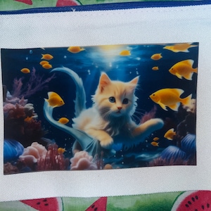 Könnte beinhalten: Eine weiße Katze mit blauen Augen und einem Meerjungfrauen-Schwanz schwimmt in einer blauen Unterwasser-Szene mit gelben Fischen. Die Katze schaut den Betrachter an.