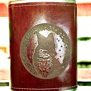 May include: A brown leather-wrapped stainless steel flask with a silver cap. The flask has an engraved design of a fox in a circle.