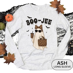 May include: Ash long sleeve shirt with a Halloween-themed graphic. The design features a ghost wearing sunglasses and a leopard print bow, holding a drink and a leopard print tote bag. The text "BOO-JEE" is above the ghost.