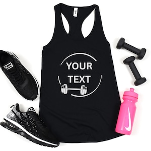 May include: A black racerback tank top featuring a white circular graphic with the text YOUR TEXT and a barbell icon. The tank top is surrounded by a pair of black athletic sneakers, two black dumbbells, and a bright pink plastic water bottle.