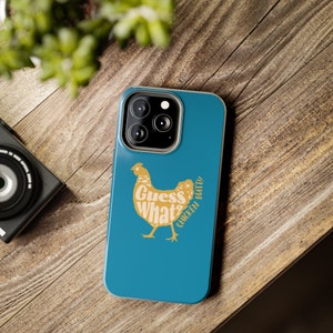 May include: A teal blue phone case with a gold chicken silhouette. The chicken is made up of the words "Guess What?" and "Chicken Bati!"