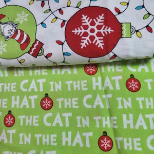 May include: Green fabric with a white repeating pattern of the text "The Cat in the Hat" and red ornaments with snowflakes.