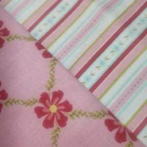 May include: Two fabric swatches. One is pink with a floral pattern of red flowers and green vines. The other is striped with pink, red, white, and light blue. The fabrics are likely cotton or a similar material.