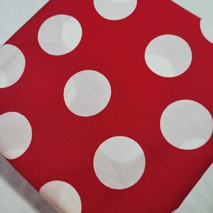 May include: A red fabric with a pattern of large white polka dots. The fabric is folded diagonally, showcasing the bold contrast between the red background and the white circles. The polka dot design is evenly spaced.