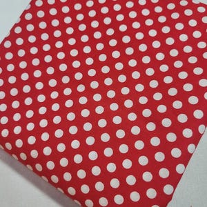 May include: Folded square of red fabric with a repeating pattern of white polka dots. The fabric is a solid red color with evenly spaced white circles. The fabric appears to be cotton or a similar material.