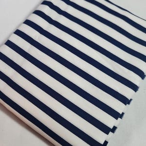 May include: Folded fabric with a pattern of navy blue and white stripes. The stripes run diagonally across the fabric. The fabric is folded over itself, showing the texture and pattern. The edges of the fabric are visible.