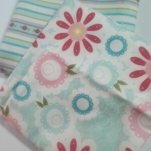 May include: Two pieces of fabric with floral and striped patterns. One fabric features large pink and blue flowers on a white background. The other fabric has horizontal stripes in light blue, pink, and green, with small floral accents.