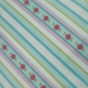 May include: A fabric with a diagonal striped pattern in shades of blue, white, pink, and green. The design includes rows of small red flowers with green leaves, and dotted lines.