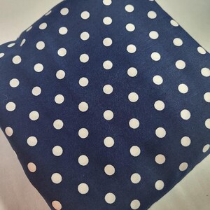 May include: A navy blue fabric with a repeating pattern of white polka dots. The fabric is folded, creating a textured appearance. The polka dots are evenly spaced and of a consistent size.