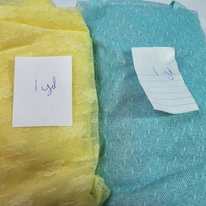 May include: Two fabric samples: one yellow and one teal. Both are textured with a floral pattern. Each has a paper tag that reads "1 yd".