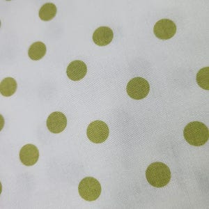 May include: White fabric with a repeating pattern of large, evenly spaced, olive-green polka dots. The dots are circular and appear to be printed on the fabric. The fabric has a slightly textured appearance.