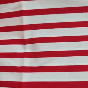 May include: Close-up of a fabric with alternating horizontal red and white stripes. The fabric has the text "Pimatex Basics" and "Screen Print" printed on it. The stripes are evenly spaced and create a bold pattern.
