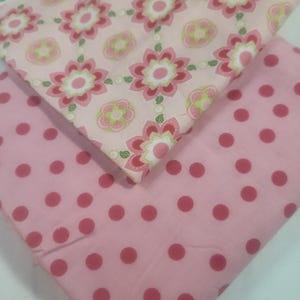May include: Two pieces of fabric. The top fabric has a pink background with a repeating floral pattern in shades of pink, red, and green. The bottom fabric is a solid pink with a pattern of large, dark pink polka dots.