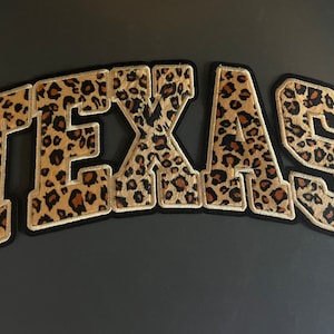 May include: A large, black and brown, leopard print patch with the word "TEXAS" in white outlined letters.