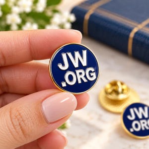 Puede incluir: Un pin de solapa redondo de esmalte con fondo azul oscuro y el texto blanco JW.ORG impreso en el centro. El pin circular tiene un borde fino de metal dorado y un mecanismo de cierre de metal dorado visible en la parte posterior.