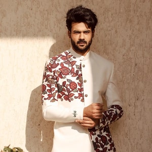 May include: A white blazer with a floral pattern on the left side and sleeve. The blazer has a mandarin collar and a single button closure.