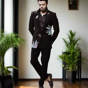 Może przedstawiać: Mężczyzna w czarnej marynarce z kwiatowym wzorem i czarnych spodniach. Ma na sobie czarne buty.