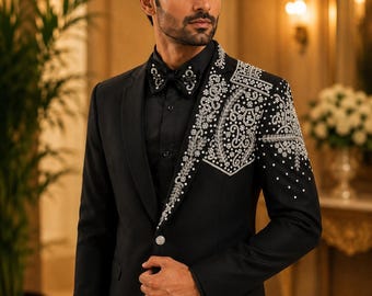 Puede incluir: Un traje negro con intrincados adornos plateados en el hombro y la solapa. El traje presenta un cierre de un solo botón y se combina con una camisa negra y una pajarita, creando un conjunto formal y elegante.