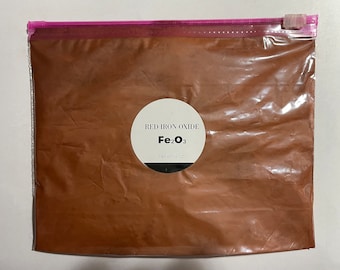 May include: A clear plastic bag with a zipper closure containing red iron oxide powder. The bag has a white label with the text "RED IRON OXIDE Fe2O3 NET WT 16 OZ".