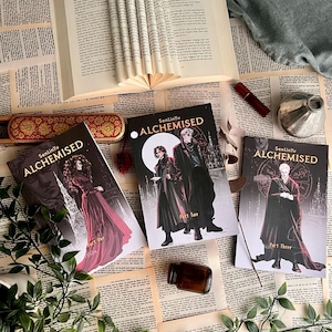 Op de afbeelding: Drie boeken getiteld "Alchemised" met gotische illustraties, naast een open boek met gevouwen pagina's. De covers tonen personages in donkere kleding. Een kleine fles en decoratieve items zijn ook aanwezig op een vintage papieren achtergrond.