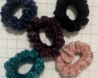 May include: Five scrunchies in different colors: teal, dark purple, black, pink, and blue. The scrunchies are made of a soft, fuzzy material.