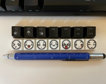 May include: A collection of black and white keyboard keycaps with various symbols and emoji faces. A blue and silver multi-tool pen with ruler markings is also present. The keycaps are arranged in rows, showcasing a unique design.