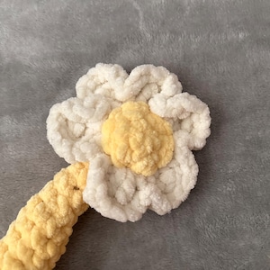 May include: A handmade crochet daisy with white petals and a yellow center. The stem is yellow. The flower is made of soft, textured yarn, perfect for a baby's toy or nursery decor.