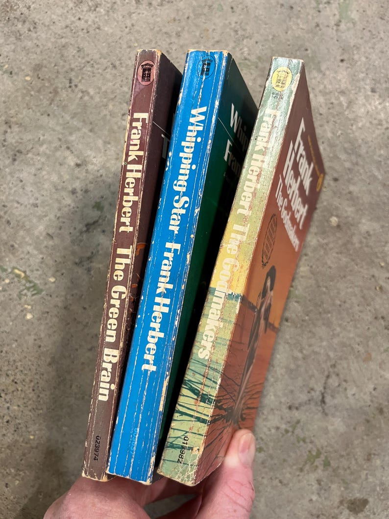 May include: Three vintage Frank Herbert paperbacks. The spines are visible, with titles including "The Green Brain," "Whipping Star," and "The Godmakers." The covers show signs of wear, with brown, blue, and orange colours.