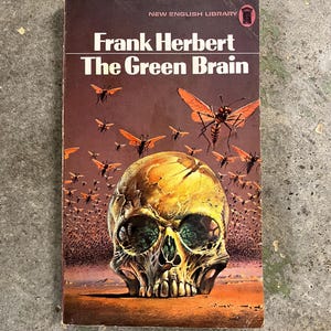 May include: A vintage paperback book titled "The Green Brain" by Frank Herbert. The cover shows a skull with green eyes and a swarm of insects with orange wings. The book is from the New English Library.