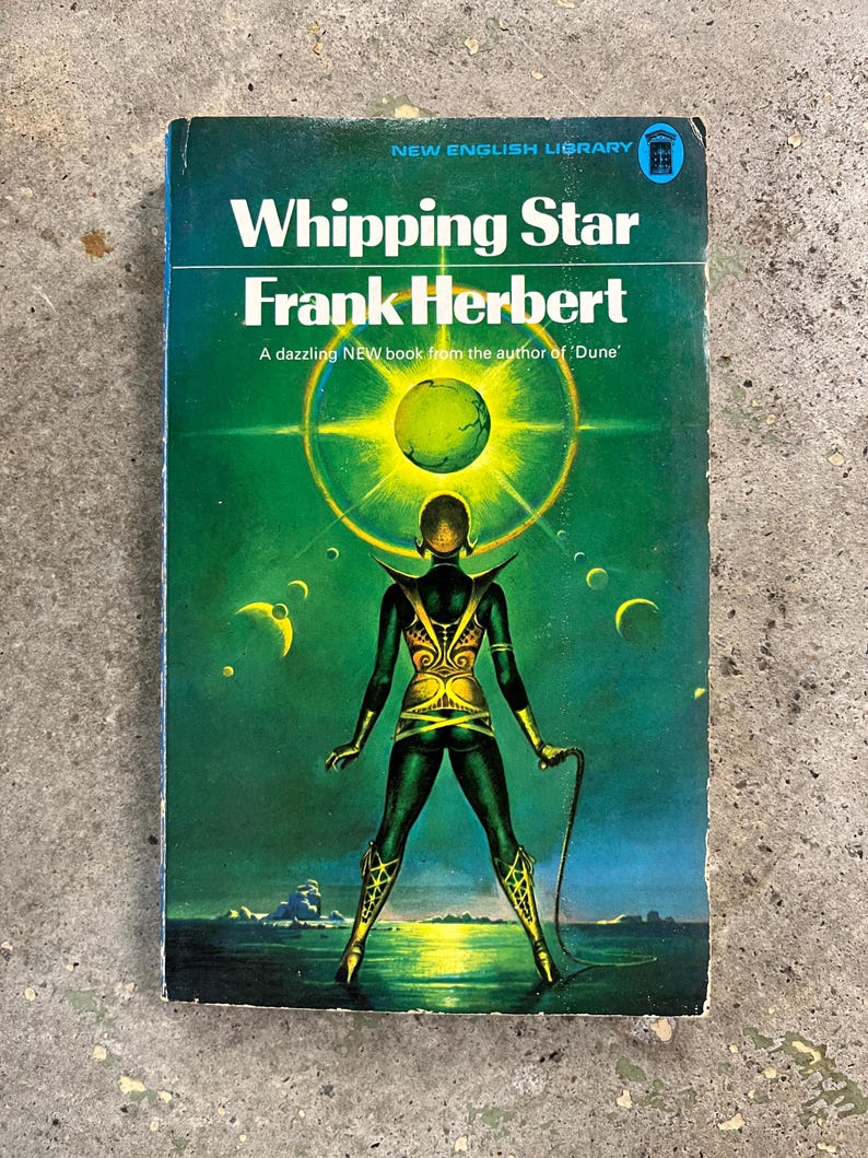 May include: Vintage paperback book cover for "Whipping Star" by Frank Herbert. The cover has a green backdrop with a figure in gold and green clothing holding a whip. The title and author's name are in white text.