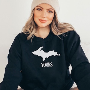 Peut inclure: Sweat-shirt noir avec un contour blanc de la péninsule supérieure du Michigan et le mot "YOURS" en dessous.