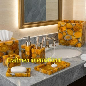 May include: A bathroom set featuring a tissue box, soap dish, toothbrush holder, soap dispenser, and a wastebasket. The set is made of a yellow and brown stone with a unique pattern. The text "Craftmen international" is visible.