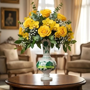 May include: A vibrant floral arrangement featuring yellow roses and orchids in a decorative white vase with green accents. The vase sits on a dark wooden table. The arrangement includes greenery and small white flowers. The vase has the text "Green International".
