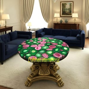 Puede incluir: Una mesa de centro redonda con una tapa de piedra de &aacute;gata verde y rosa. La mesa tiene una base dorada con detalles de cabeza de carnero. La habitaci&oacute;n cuenta con sof&aacute;s azules, cortinas color crema y una alfombra blanca.