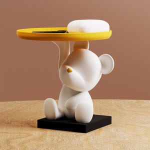 Peut inclure: Une figurine d'ours en céramique blanche tenant un plateau jaune avec un porte-savon blanc sur le dessus. L'ours est assis sur une base noire.
