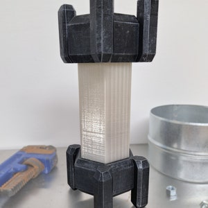 以下が含まれることがあります： 黒いベースと白のテクスチャ加工された中央部分を持つ3Dプリントされたタワー。タワーは六角形の形をしており、装飾的な尖ったトップで設計されています。